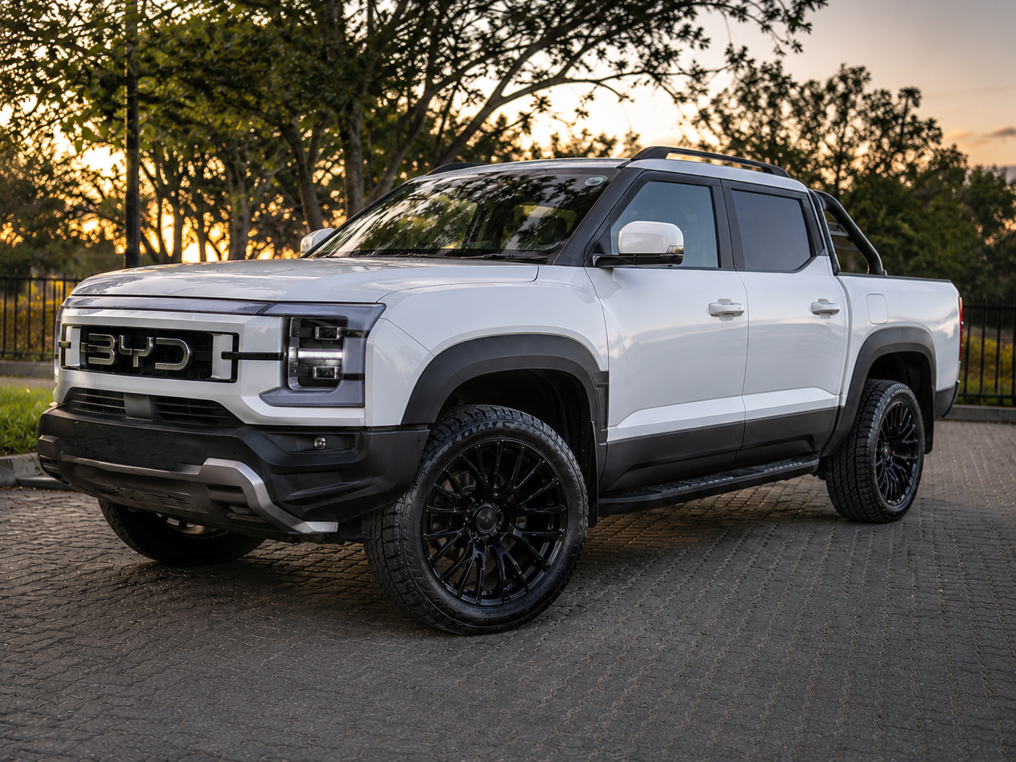 White BYD Shark pickup truck fitted with 17 inch black multi-spoke alloy wheels and new tyres in an outdoor setting